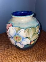 Front view showing floral motifs on vase with magnolia flowers and green leaves on cream and blue background.