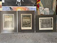 Three framed and matted prints leaning against a wall, one print glass cracked on the middle frame.