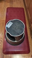 Kik Step Cramer metal step stool positioned atop rectangular red cushioned mat on wooden floor.