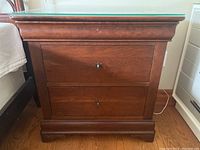 Front view of solid wood side table showing two drawers with metal knobs and a decorative base.