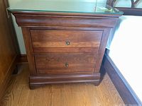 Front view of the wood side table showing glass top and two drawers with metal handles.