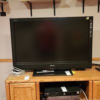Front view of Sony Bravia 40 inch TV on a wooden table with remote on stand base.