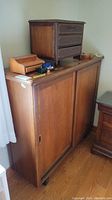 View of the full vintage cabinet showing two sliding doors and a top surface with small wooden items placed on it but excluded from the lot.