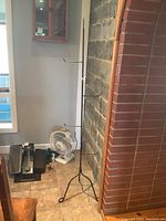 Full view of the tall black metal rack standing on a tiled floor next to a stone wall and brick column, showing the overall structure and base tripod legs.