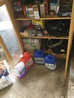 Shot of the lower shelves holding various automotive cables, fuel jugs and other supplies stored inside a wooden cabinet.