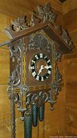 Front view of entire carved wooden cuckoo clock hanging on wall with weights and chains visible