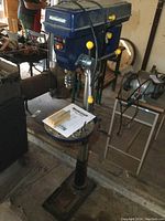 Full front view of the drill press with table and base, includes manual on table