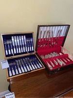 Two wooden canteens side by side: left with Ambrose Kent fish flatware set, right with Rogers Bros flatware service