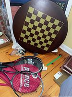 Reversible wooden game board showing Checker board side with checkers pieces and tennis rackets in front.