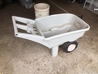 Side view of the gray Rubbermaid garden cart with two wheels and integrated handles, showing dirt inside basin.
