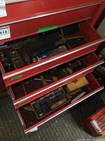 Three red tool drawers open showing assorted small hand tools in lower three drawers