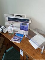 Machine on wooden table with quilting shelf, instruction manual and small accessories laid out