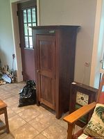 Full view of the wooden jam cupboard showing the door with knob and top molding, placed in a tiled floor room next to a door.