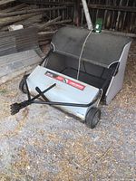 Front view of assembled tow-behind lawn sweeper showing metal housing, hitch and fabric hopper.