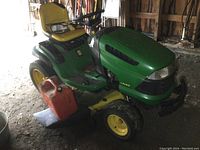 Angled front-side view showing tractor body, seat, mower deck and red fuel can alongside.
