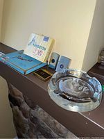 Overview photo of Kingston 300 cigarette pack, metal Platers box, three propane lighters, and glass ashtray on mantle.