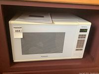 White Panasonic microwave oven placed inside a wooden shelf with a control panel on the right side and a digital clock display showing 11:56.