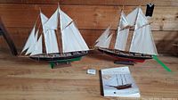 Lot including two model sailing ships and a book on model boats placed on a wooden floor with wood panel background.