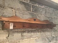 Full view of the wooden colonial style peg coat rack mounted on a stone wall, showing the 6 pegs and shelf.