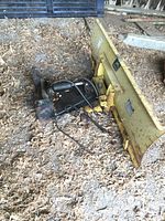 Angled overview of the yellow curved blade assembly with hydraulic hoses and mounting bracket