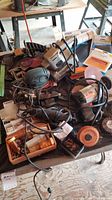 Photo of various power tools including B&D corded drill, Craftsman rotary tool, Black & Decker Mouse sander, ShppCraft orbital sander, drill bits and sandpaper spread on a workbench.