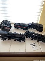 Lionel 027 steam locomotive and tender along with transformer and plastic train cars on a white surface near window light.