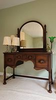 Front view of vintage wooden vanity with swivel mirror and three drawers, showing ornate wood pulls and turned legs.