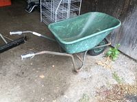 Wheelbarrow angled side view showing green resin tub, metal black frame, and handles.