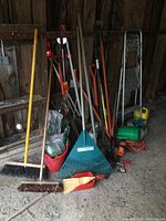Overview of yard tools including brooms, rake, stakes, electric hedge trimmer and foldable ladder inside a wooden shed