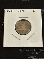 Obverse of 1858 US Flying Eagle cent showing eagle in flight with date 1858 below, stapled in cardboard coin holder.