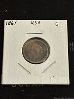 Front side of 1861 Indian Head penny in white paper coin holder.