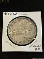 Reverse side of 1953 Canadian silver dollar showing birch bark canoe design with voyageurs and denomination details.