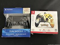 Front view of the Sony PS4 DualShock 4 wireless controller in original packaging and Nintendo Switch wired Pokémon themed controller in original packaging