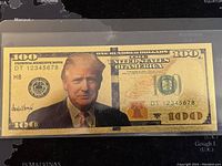 Front view of the 24K gold foil novelty bill featuring a colored portrait of Donald Trump, serial number DT 12345678, with denomination 100 and United States of America text.