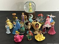 Full lot overview showing all 21 pieces of Disney princess figurines and Tinker Bell musical globe centered in background.
