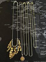 Five sterling silver necklaces laid flat on a map background, showing the overall variety and length of necklaces in the lot, including a unique gold-tone charm necklace and four fine chains.
