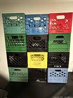 Front view of stacked assorted plastic storage and moving crates in various colors showing details of patterns, handles, and condition.