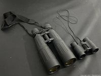 Both large 8x56 and small 4x30 binoculars placed side-by-side on black cloth background showing size difference and attached straps.
