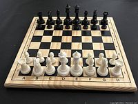 Chess set arranged on black surface, board showing black and white pieces in starting positions.
