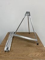Aluminum tripod table easel set up with support ledge on wooden surface.