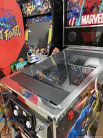 Three-quarter front view showing glass-covered LCD playfield, side Marvel artwork and chrome trim