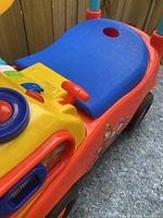 Close-up angle showing blue seat, yellow steering wheel, and red body with stickers.