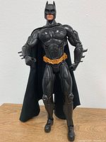 Front view of Batman figurine showing full body with muscular chest, yellow utility belt, and black cape.