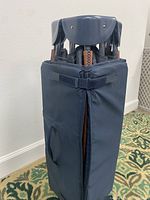 Folded child’s play/sleep pen covered in navy blue fabric with carrying handle and velcro strap.