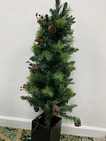 Full view of the artificial Christmas porch tree with pinecones and red berries in a black planter.