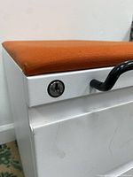 Close-up image showing the orange cushioned seat and locking mechanism on the upper drawer of the white metal cabinet.
