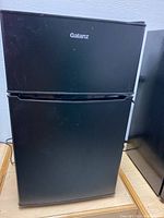 Front view of black Galanz mini fridge with freezer section on top and fridge below.