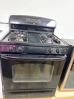 Front view of the GE black gas stove with oven, showing four burner tops and control handles with digital panel.