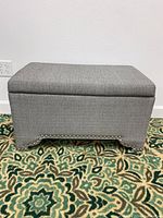 Front view of a rectangular grey storage bench with nailhead trim