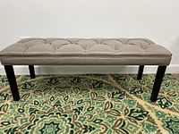 Full view of the griege bench with tufted cushioned seat and dark legs, showing overall design and structure.